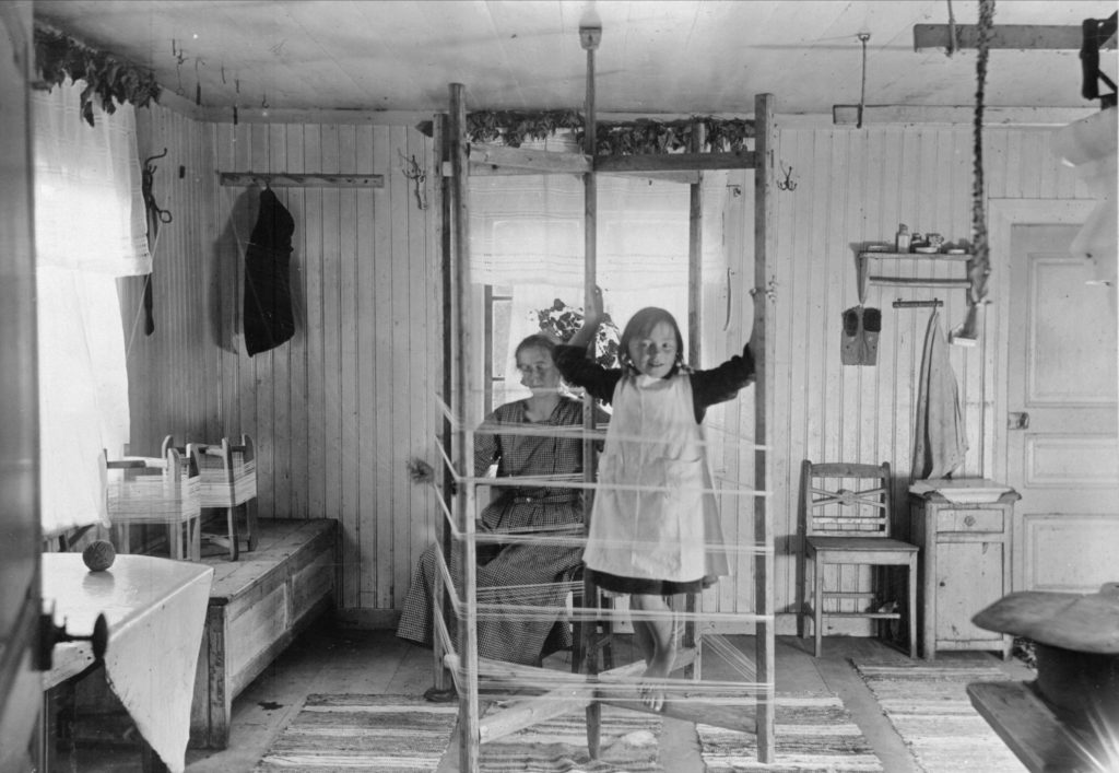 Gammal interiör i finngård. Flicka klättar på en varpställning.